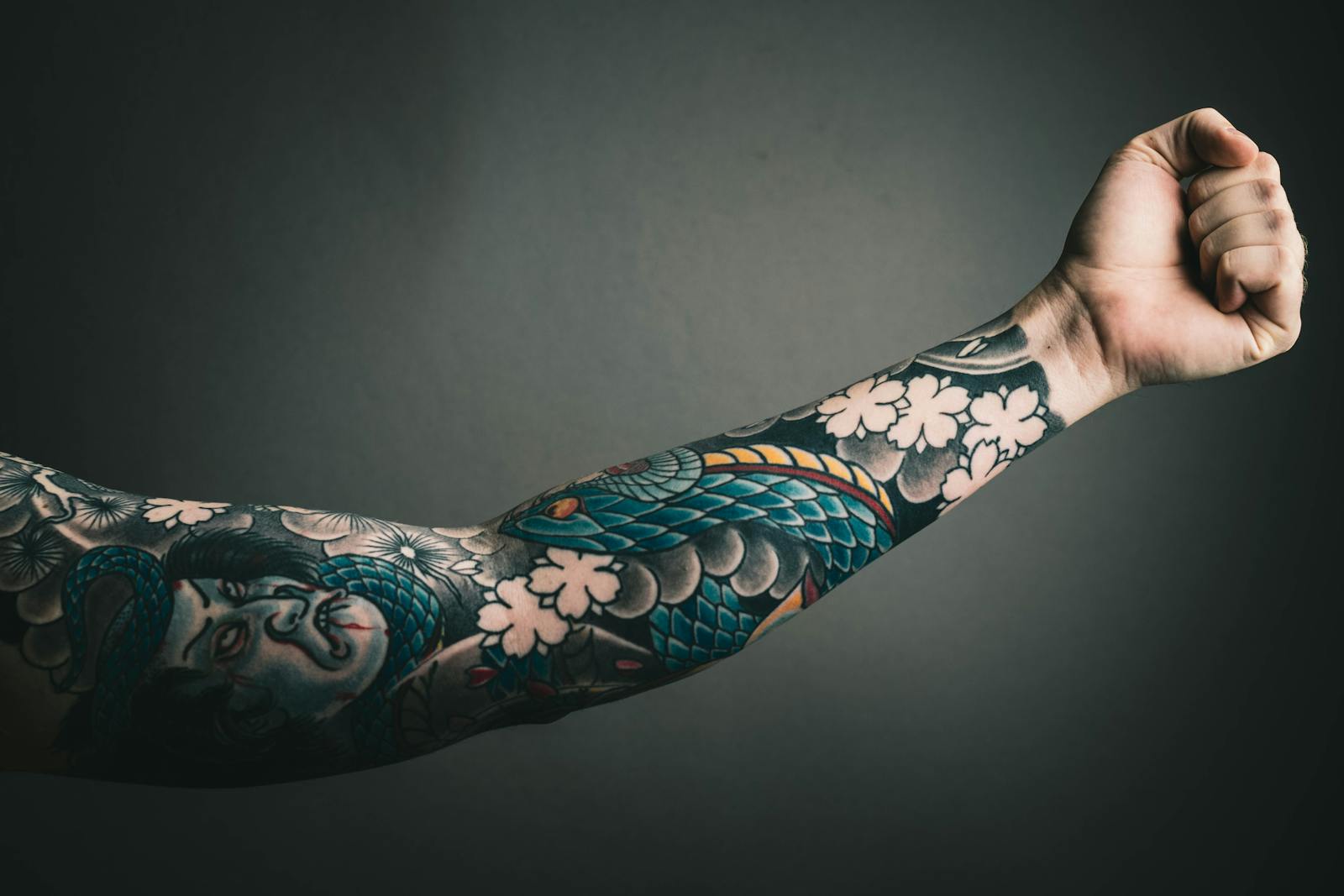 A close-up of a tattooed arm with a colorful sleeve design, featuring floral and artistic elements.