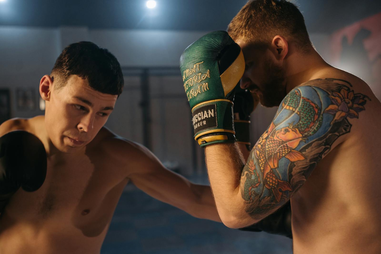 Two shirtless boxers sparring in a gym under focused lighting.